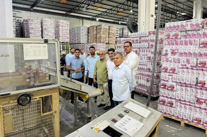 Foto mostra homens olhando para uma máquina em operação dentro de uma empresa de papel