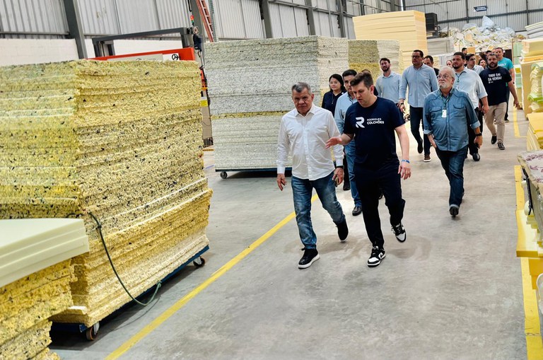 Foto mostra pessoas caminhando dentro de uma fábrica de colchões