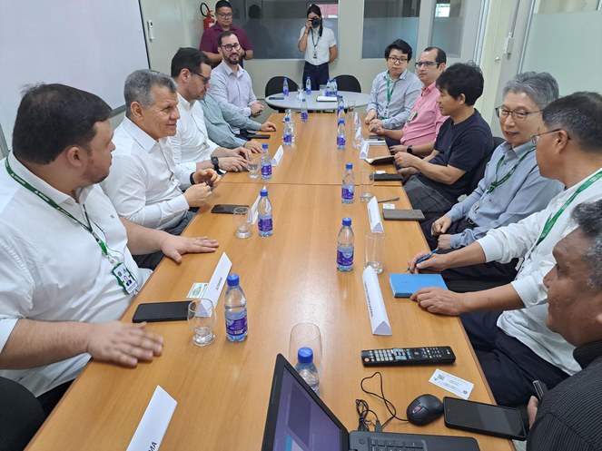 Foto mostra um grupo de homens sentados à mesa em uma reunião