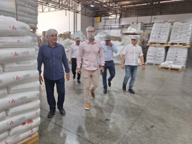 Foto mostra grupo de homens com toca branca na cabeça em visita a uma linha de produção de embalagem plástica