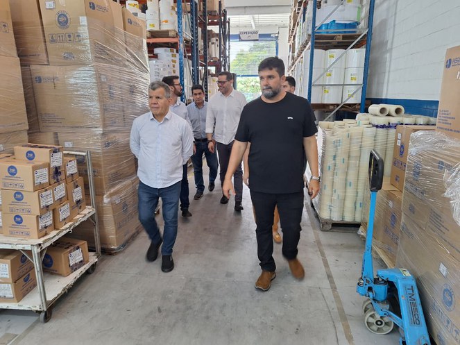 Foto mostra homens caminhando em meio a caixas de papelão e produtos adesivos