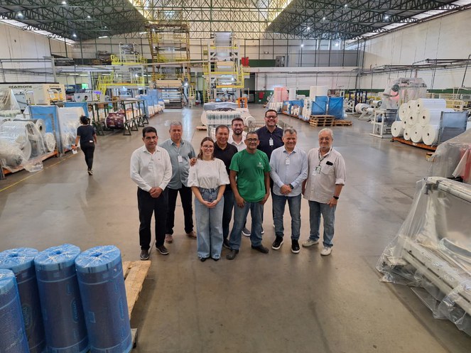 Foto mostra um grupo de pessoas visitando uma fábrica de produtos de embalagens plásticas