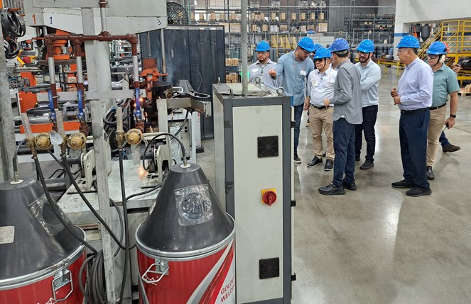 Foto mostra grupo de homens com capacete azul em uma fábrica de botijas de gás