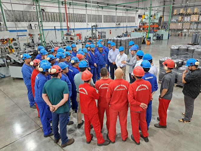 Foto mostra homens de capacete em uma fábrica de botijas de gás