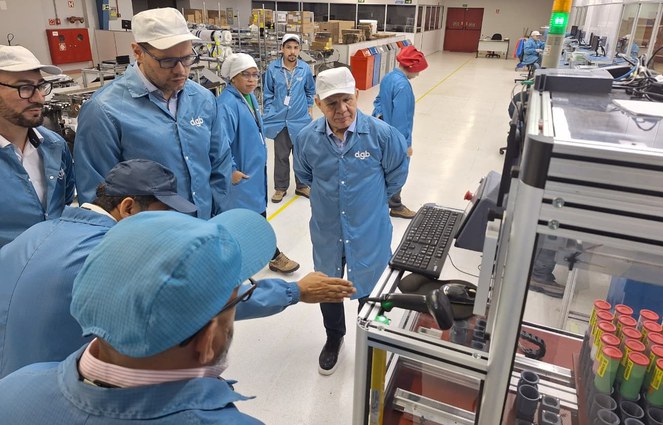 Foto mostra homens de bata azul olhando para uma máquina