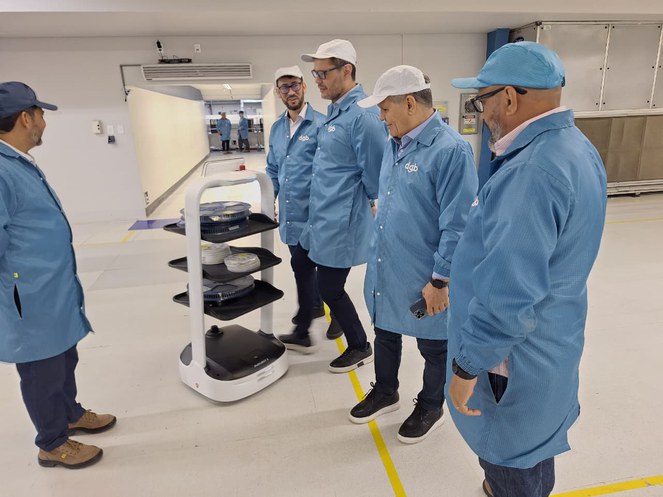 Foto mostra homens de bata azul olhando para uma máquina em movimento