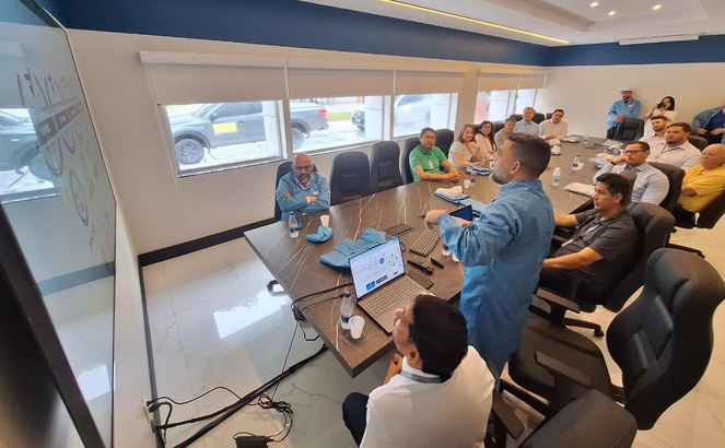 Foto mostra homem em pé fazendo uma explanação numa reunião para outras pessoas