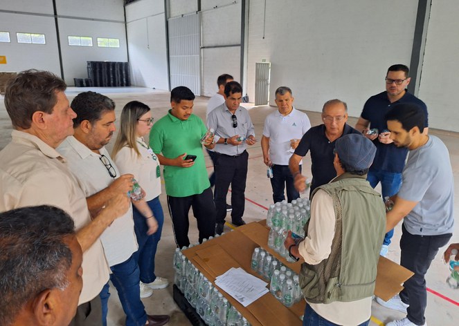 Foto mostra homens segurando e conferindo qualidade de garrafas de água mineral