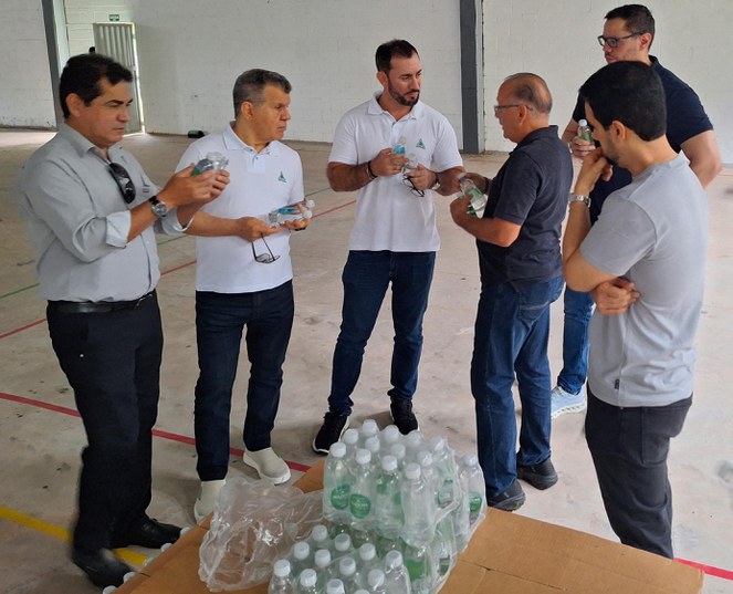 Foto mostra uns homens segurando e conferindo qualidade de garrafas de água mineral