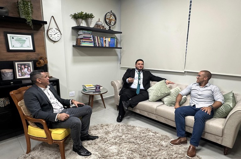 Foto mostra homem de paletó e gravata falando com outros dois homens