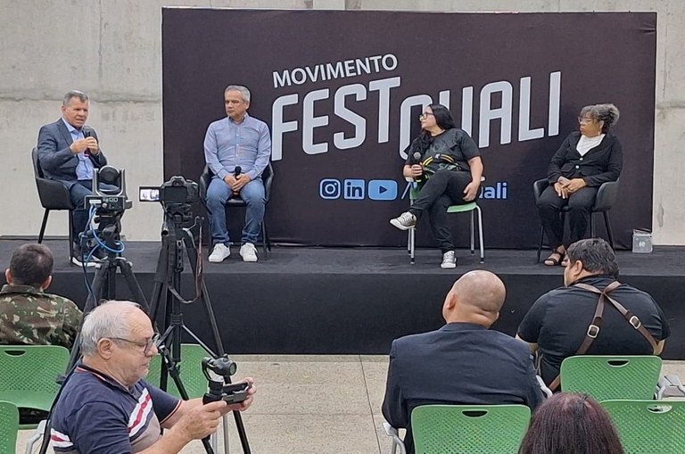 Foto mostra homem falando ao microfone em um evento
