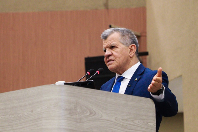 Foto mostra homem de blazer azul falando ao microfone