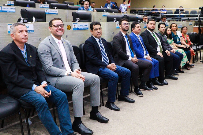 Foto molstra grupo de pessoas sentadas em evento oficial