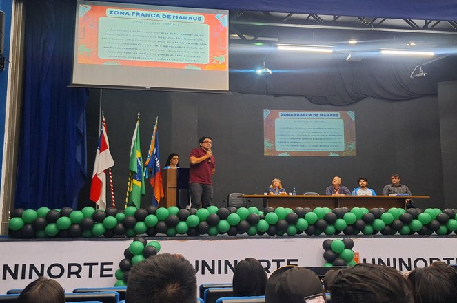 Foto mostra homem de blusa vermelha e microfone na mão falando em público