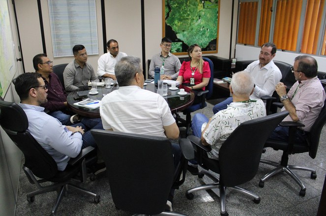 Foto mostra pessoas reunidas numa sala, com mapas na parede ao fundo