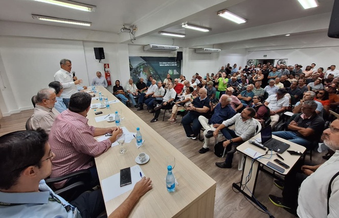Foto mostra homem em pé falando ao microfone em um auditório lotado
