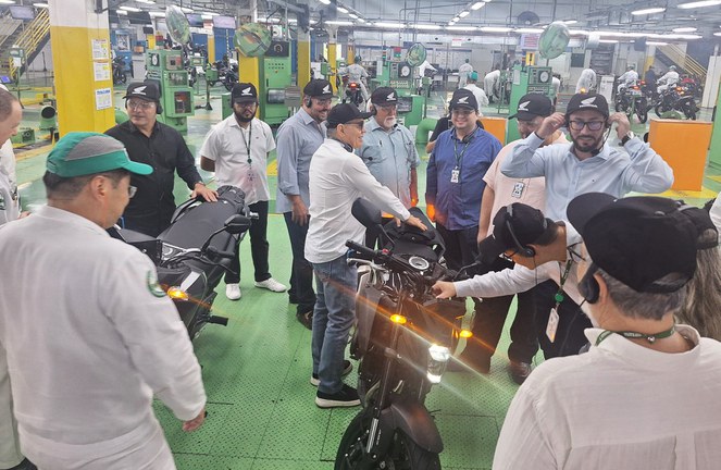 Foto mostra grupo de homens verificando motocicletas à mostra dentro de uma fábrica