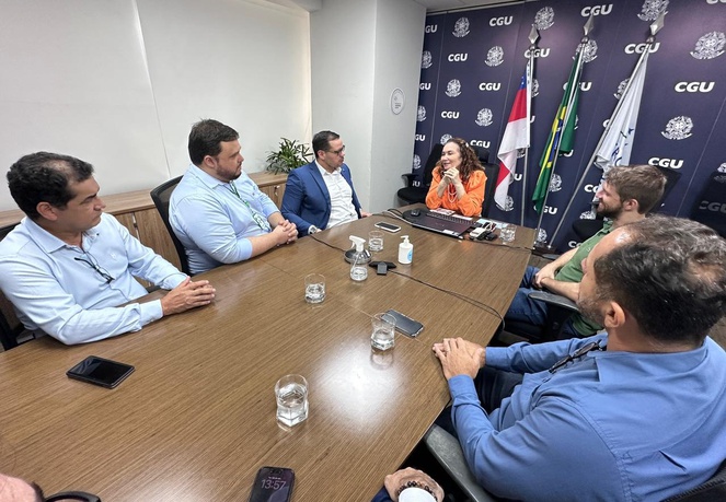 Foto mostra pessoas sentadas à mesa numa reunião