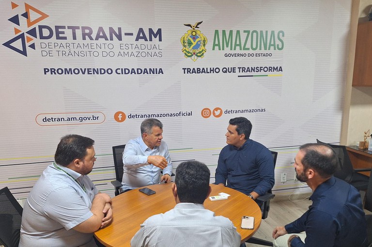 Foto mostra pessoas sentadas à mesa em reunião de trabalho