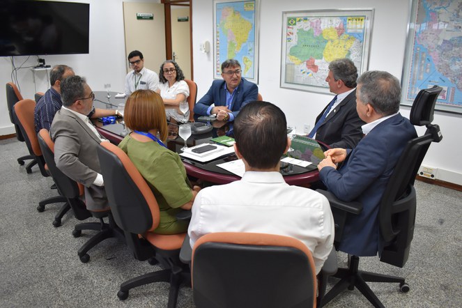 Foto mostra homem de blazer azul fazendo uma explicação durante reunião com grupo de pessoas