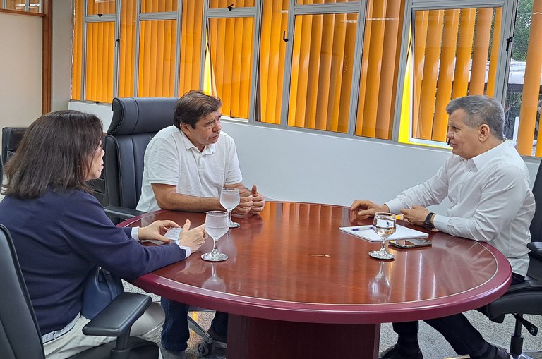 Foto mostra três pessoas sentadas à mesa em reunião