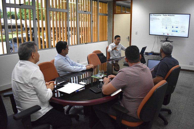 Foto mostra homem de blusa branca e usando óculos fazendo uma explanação para outros quatro homens