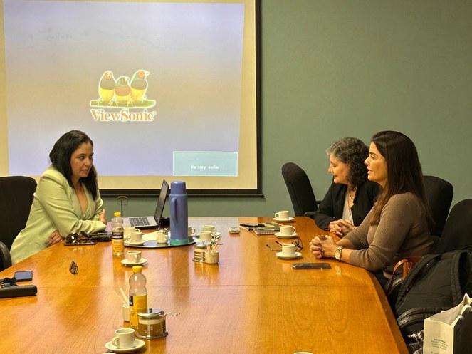 Foto mostra três mulheres sentadas e um telão de fundo