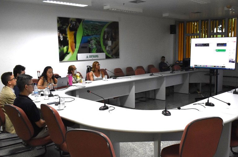 Foto mostra pessoas olhando para uma televisão, durante uma reunião por videoconferência