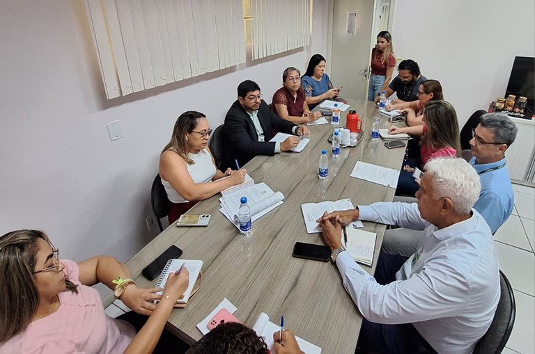 Foto mostra pessoas sentadas à mesa em uma reunião