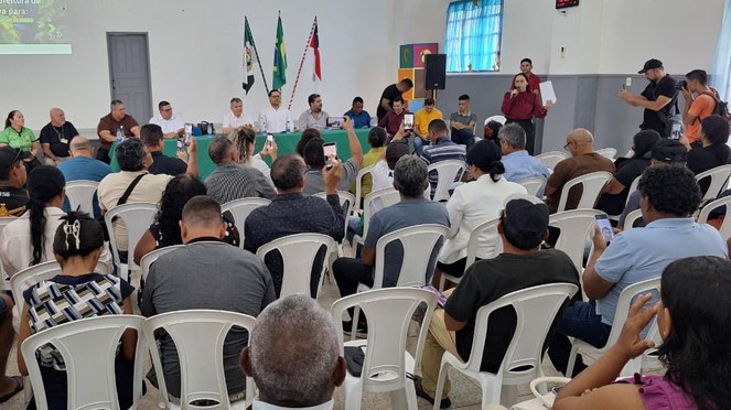 Foto mostra mulher falando em evento público com um papel na mão