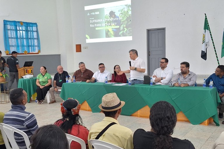 Foto mostra homem de blusa branca falando ao microfone em um evento