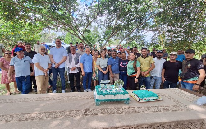 Foto mostra pessoas posando para foto, com um bolo confeitado no primeiro plano