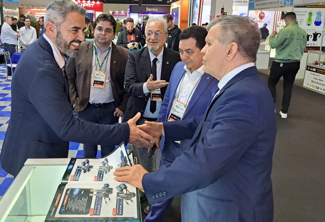 Foto mostra dois homens de paletó apertando as mãos, observados por outros três homens