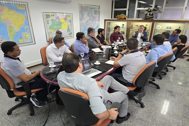 Foto mostra um homem gesticulando durante explanação numa reunião com outras pessoas