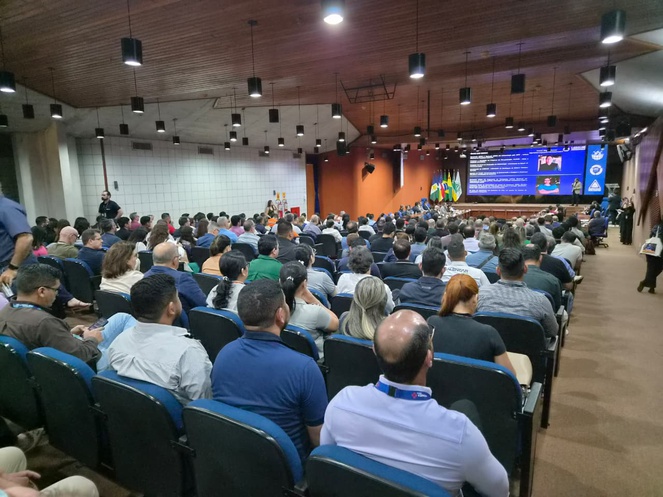 Foto mostra auditório lotado num evento e um telão ao fundo