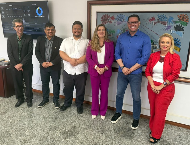 Foto mostra pessoas em pé posando para foto com quadros ao fundo
