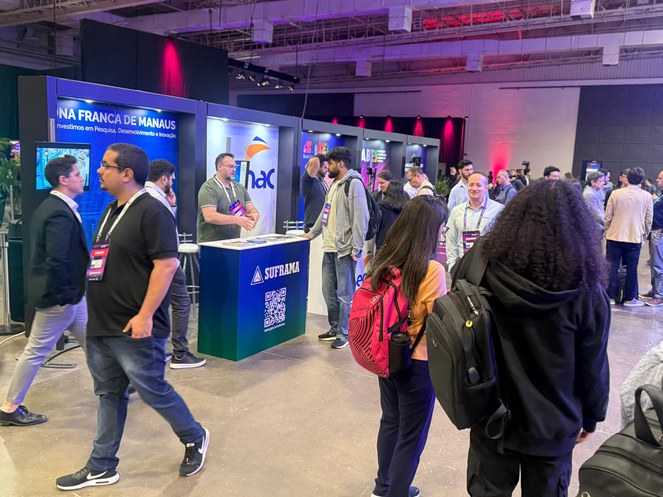 Foto mostra homem de blusa verde prestando atendimento em um estande a outro homem