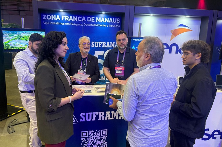 Foto mostra mulher conversando com homem de posse de uma cartilha, observados por outros homens