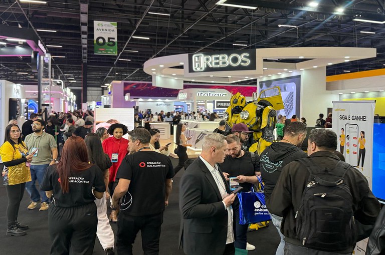 Imagem mostra várias pessoas andando no pavilhão de evento da feira