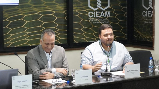 Foto mostra homem falando ao microfone ao lado de outro homem