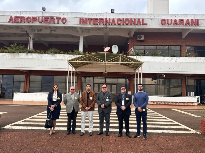 Foto mostra grupo de pessoas posando para foto na fachada de um aeroporto no Paraguai