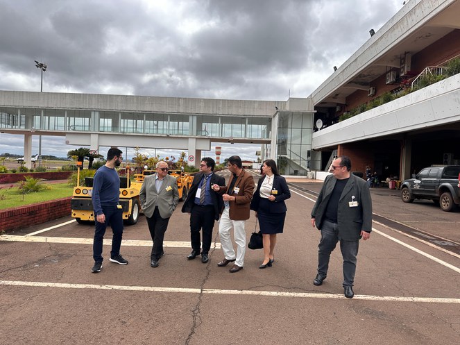 Foto mostra pessoas caminhando com veículos utilitários amarelos ao fundo