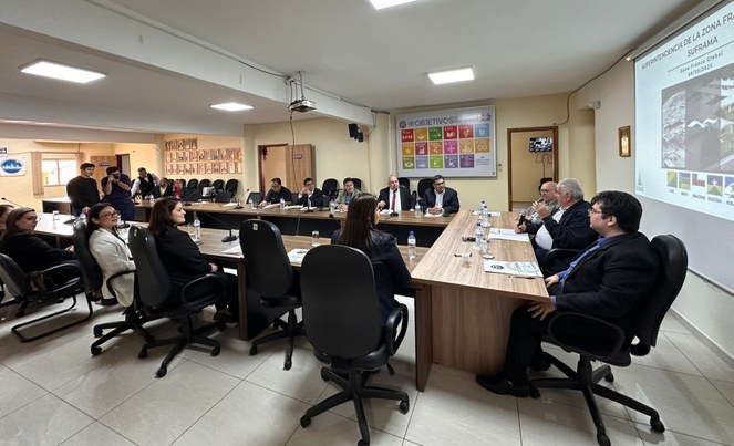 Foto mostra grupo de pessoas em uma reunião, com um telão como apoio