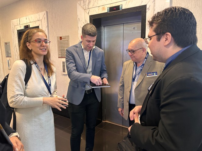 Foto mostra mulher de blazer claro conversando com dois homens