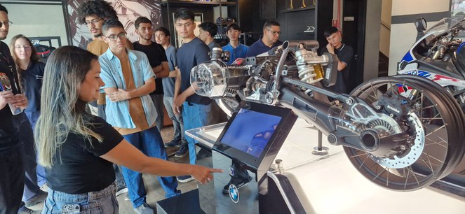 Foto mostra mulher mostrando produção de motocicletas a grupo de universitários