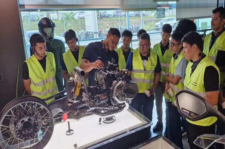 Foto mostra pessoas de jaqueta olhando para uma motocicleta em produção