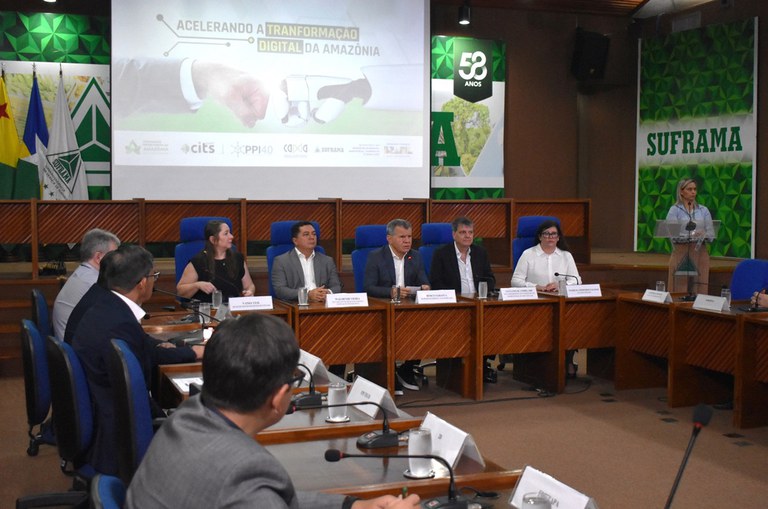 Foto mostra pessoas num evento realizado em um auditório com um telão ao fundo