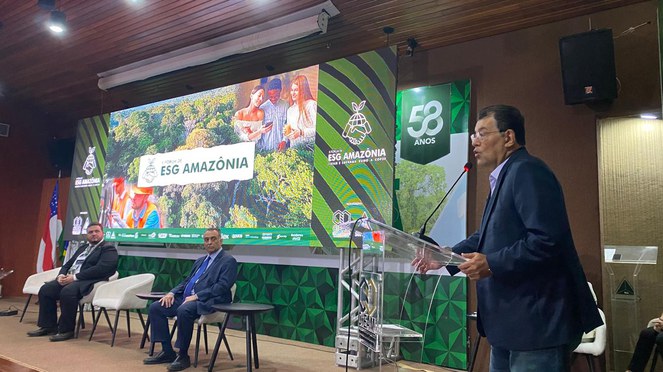 Foto mostra homem de paletó azul escuro falando em evento público