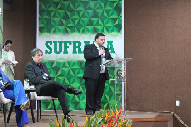 Foto mostra homem vestido com paletó preto e microfone na mão, falando em público