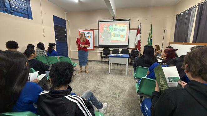 Uma mulher em uma sala de aula, de pé, apresentando para os alunos